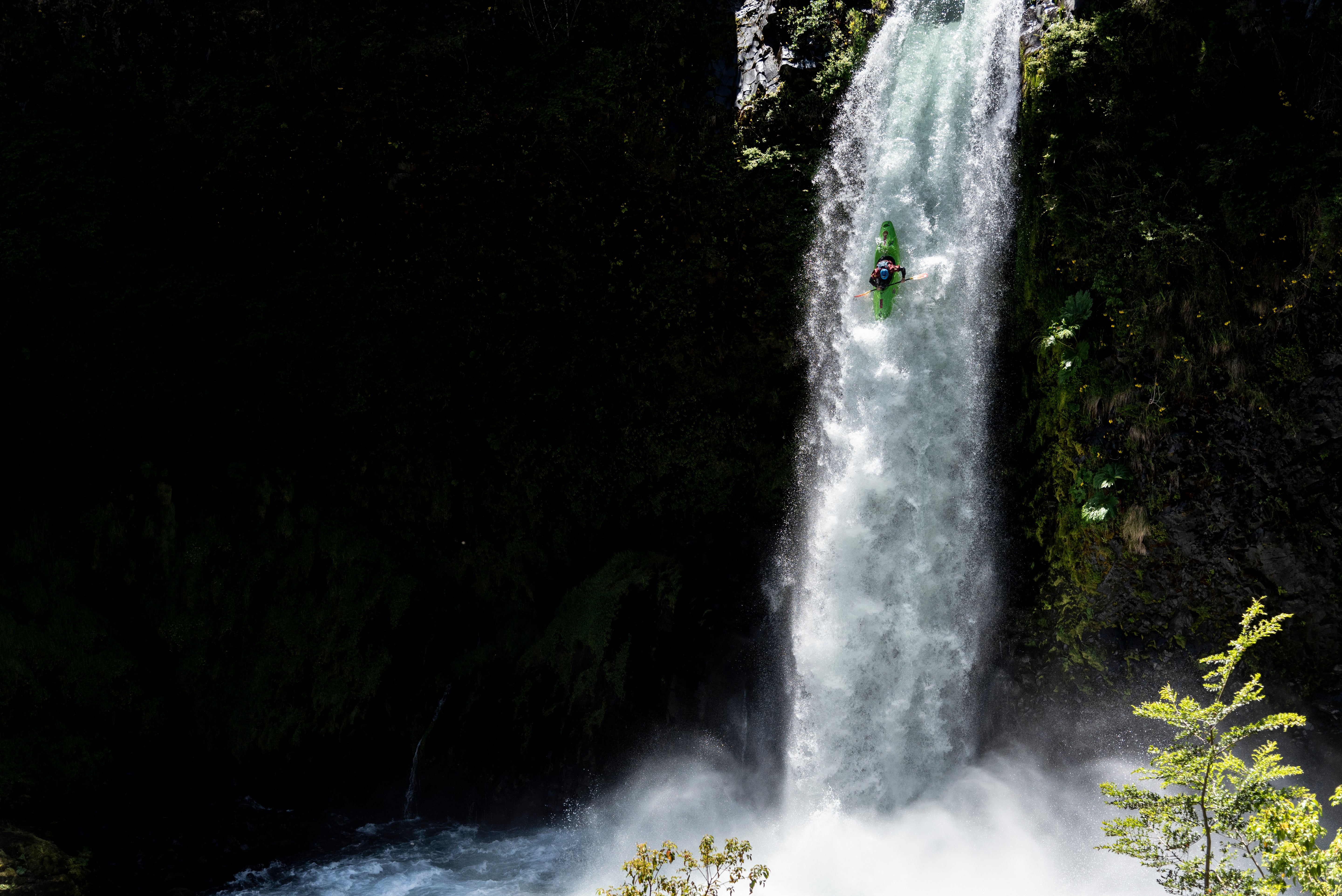 Person rappelling down a waterfall in a forested area