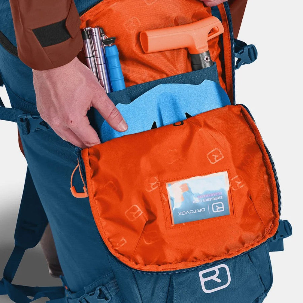 Orange backpack with visible brand logo, contents including a blue water bottle and black tool, on a gray background.