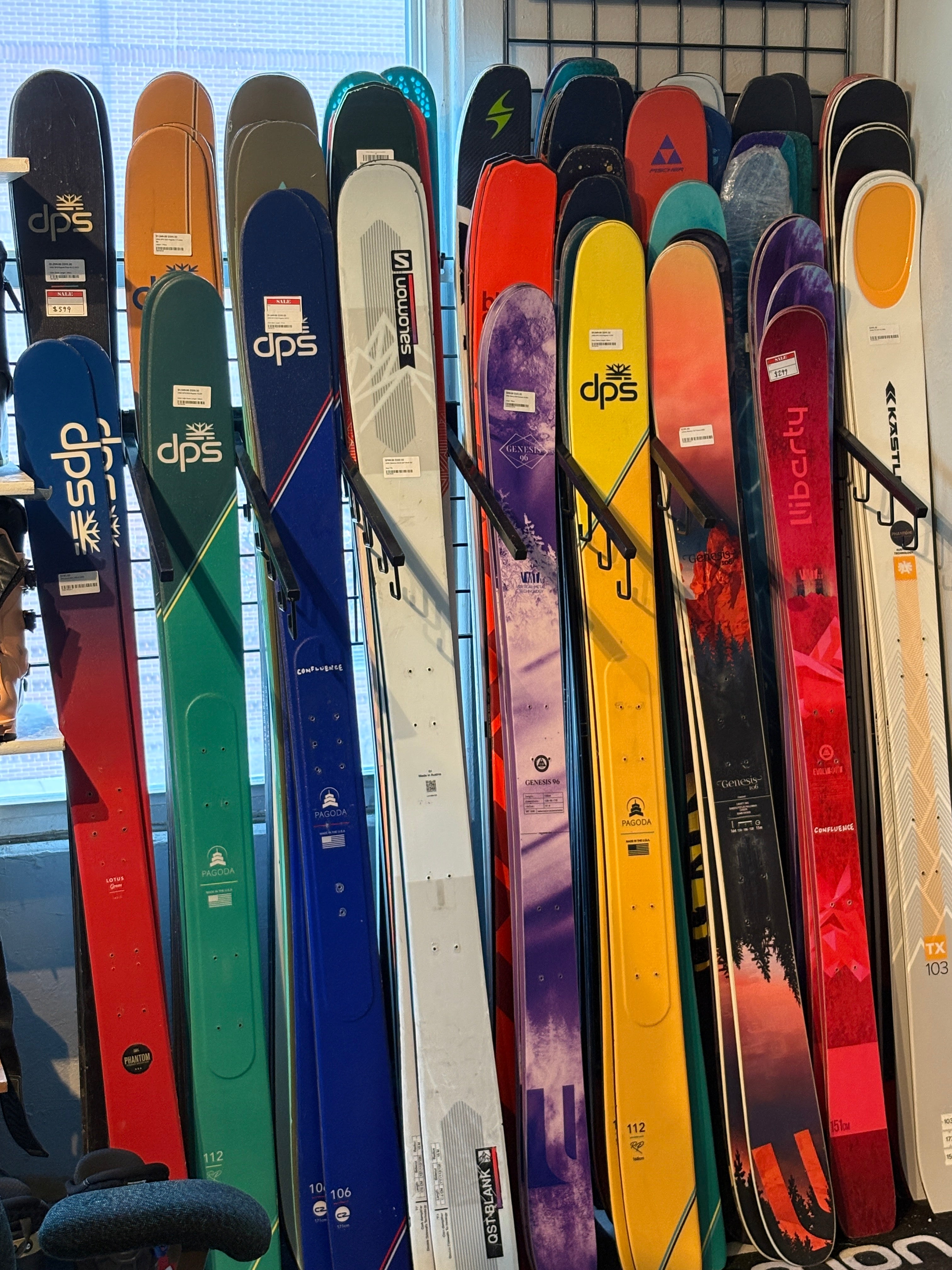 Stack of colorful skis with various brands on a tiled floor.